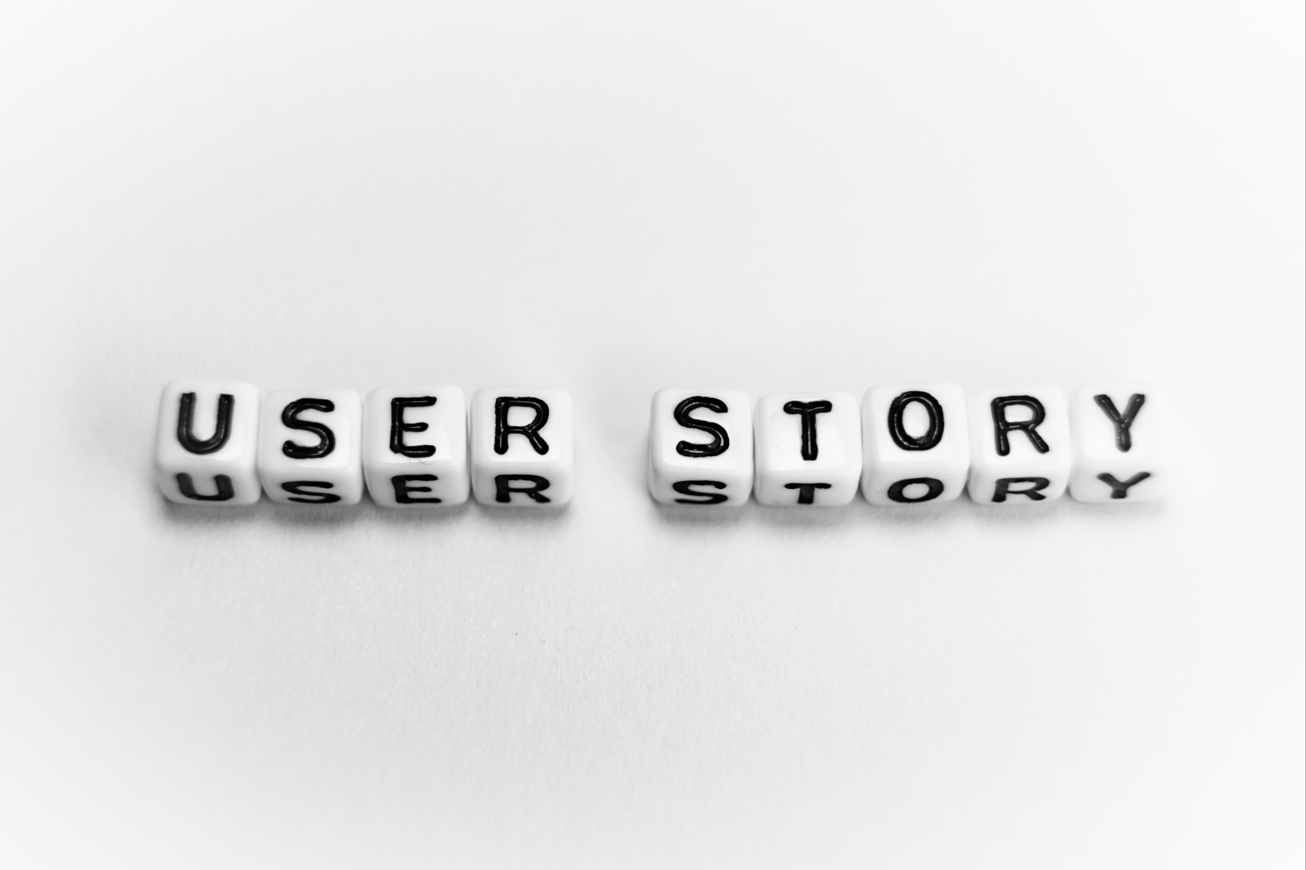 The image shows white dice-like blocks with black letters spelling out "USER STORY" arranged in two rows. The top row spells "USER" and the bottom row spells "STORY," making the phrase "USER STORY" prominent and clear.